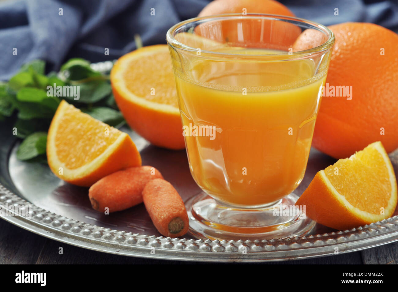 Orange und Karotten-Saft im Glas mit Minze, frisches Obst und Gemüse auf rundes Tablett Stockfoto