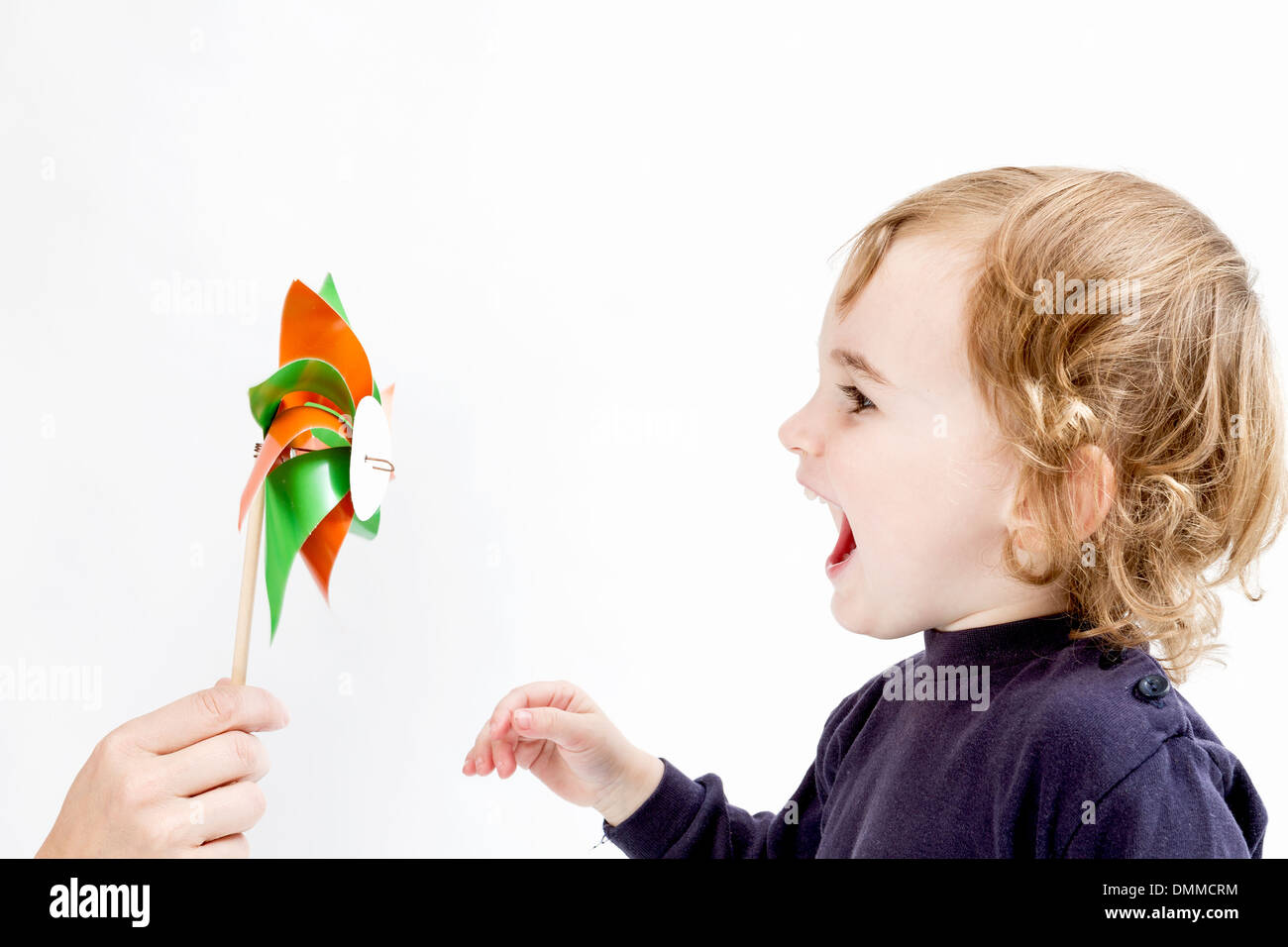 niedliche Mädchen bläst, bunte Windmühle. Studio in hellen grauen Hintergrund gedreht Stockfoto