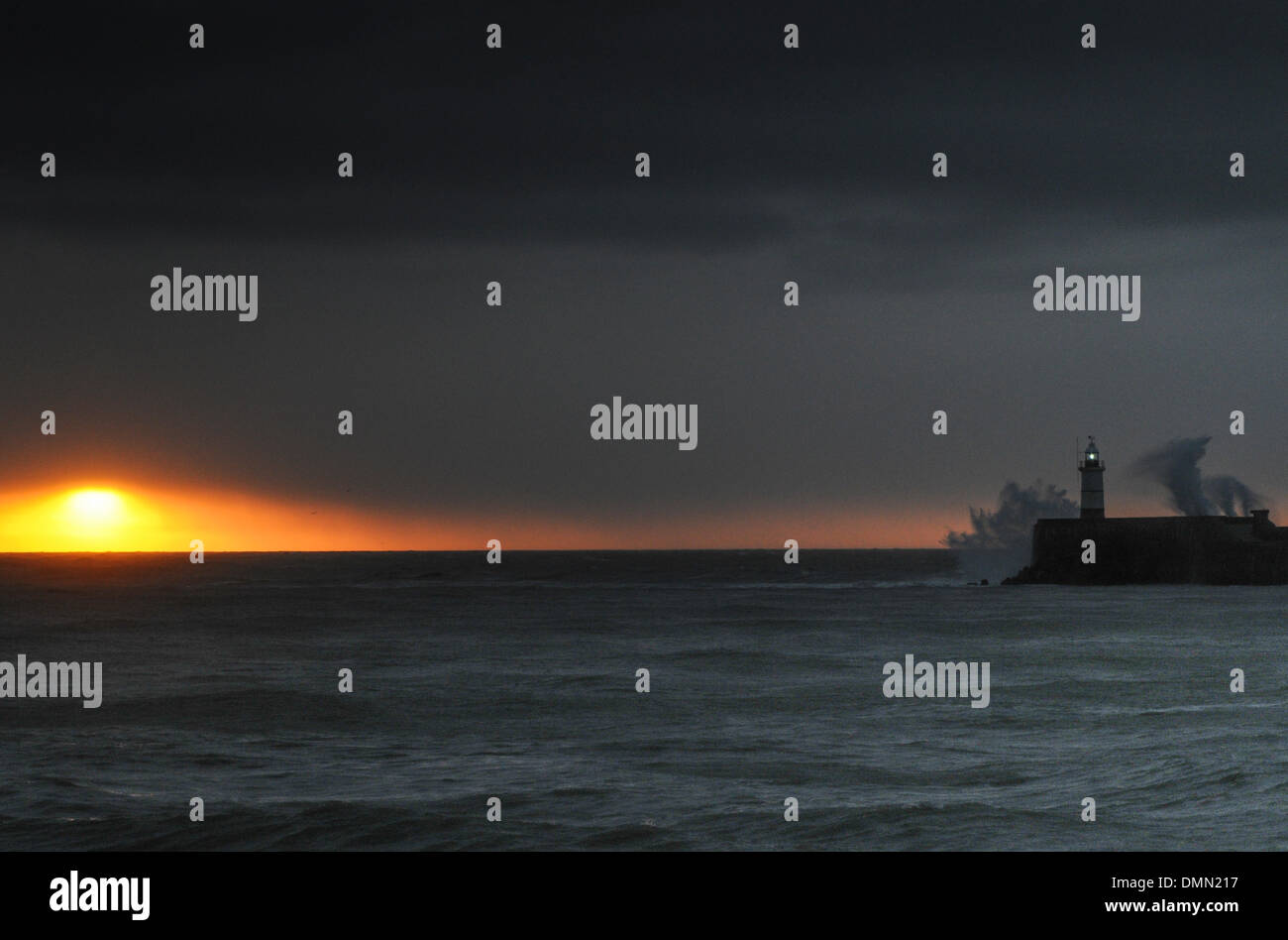 Newhaven, Sussex, UK. 16. Dezember 2013. Sonnenaufgang für kurze Zeit als Wolken und Regen Ansatz sichtbar. Orkanartigen Winden schüren die Wellen, die über den Westarm in Newhaven abstürzen. Bildnachweis: David Burr/Alamy Live-Nachrichten Stockfoto