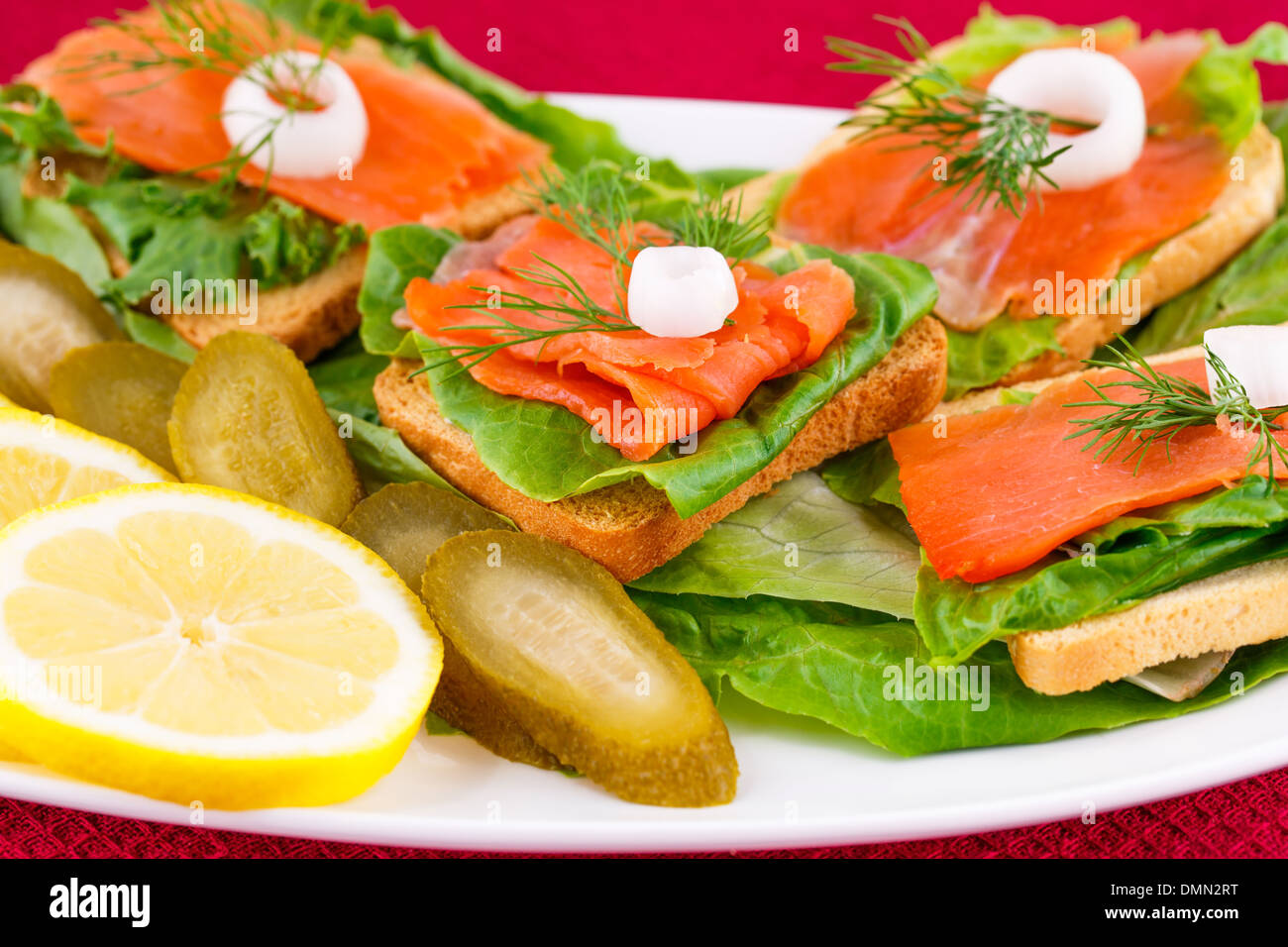Lachs Sandwiches mit Salat, frische und eingelegte Gurken, Zwiebel, Zitrone auf Platte. Stockfoto