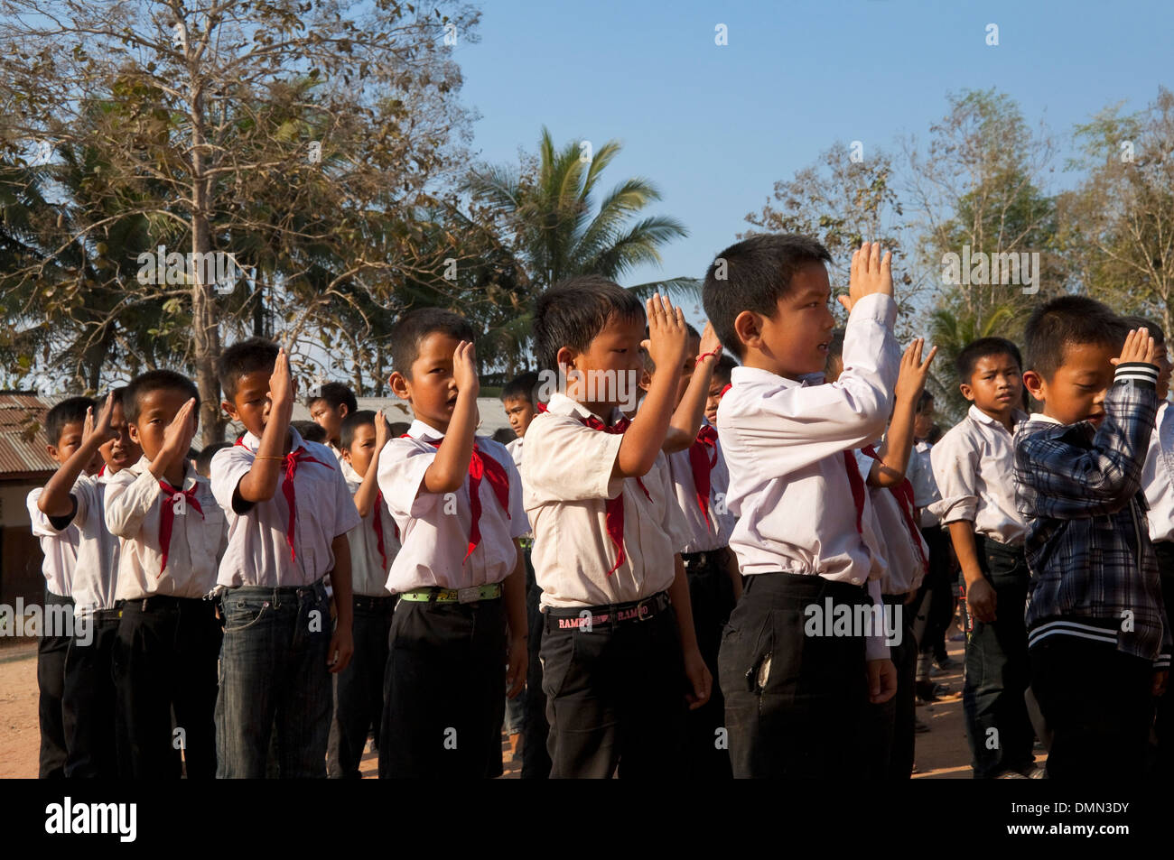 Horizontale Ansicht von Schulkindern salutieren und gemeinsam zu singen, während ihre Fahne heben an einer Schule in Laos. Stockfoto