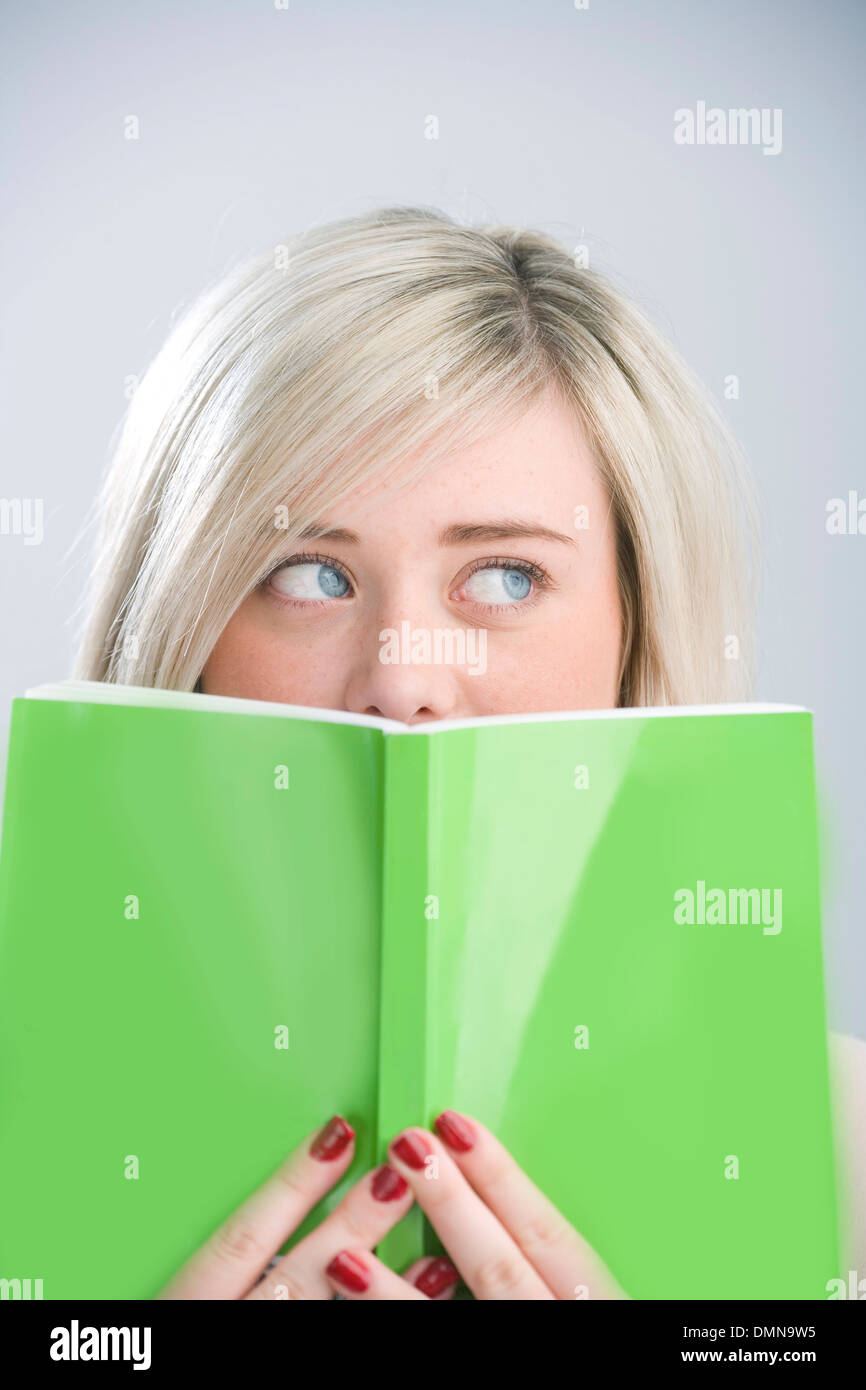 Hübsche blonde Teenager peeking über ein grünes Buch hielt vor ihr Gesicht. Stockfoto