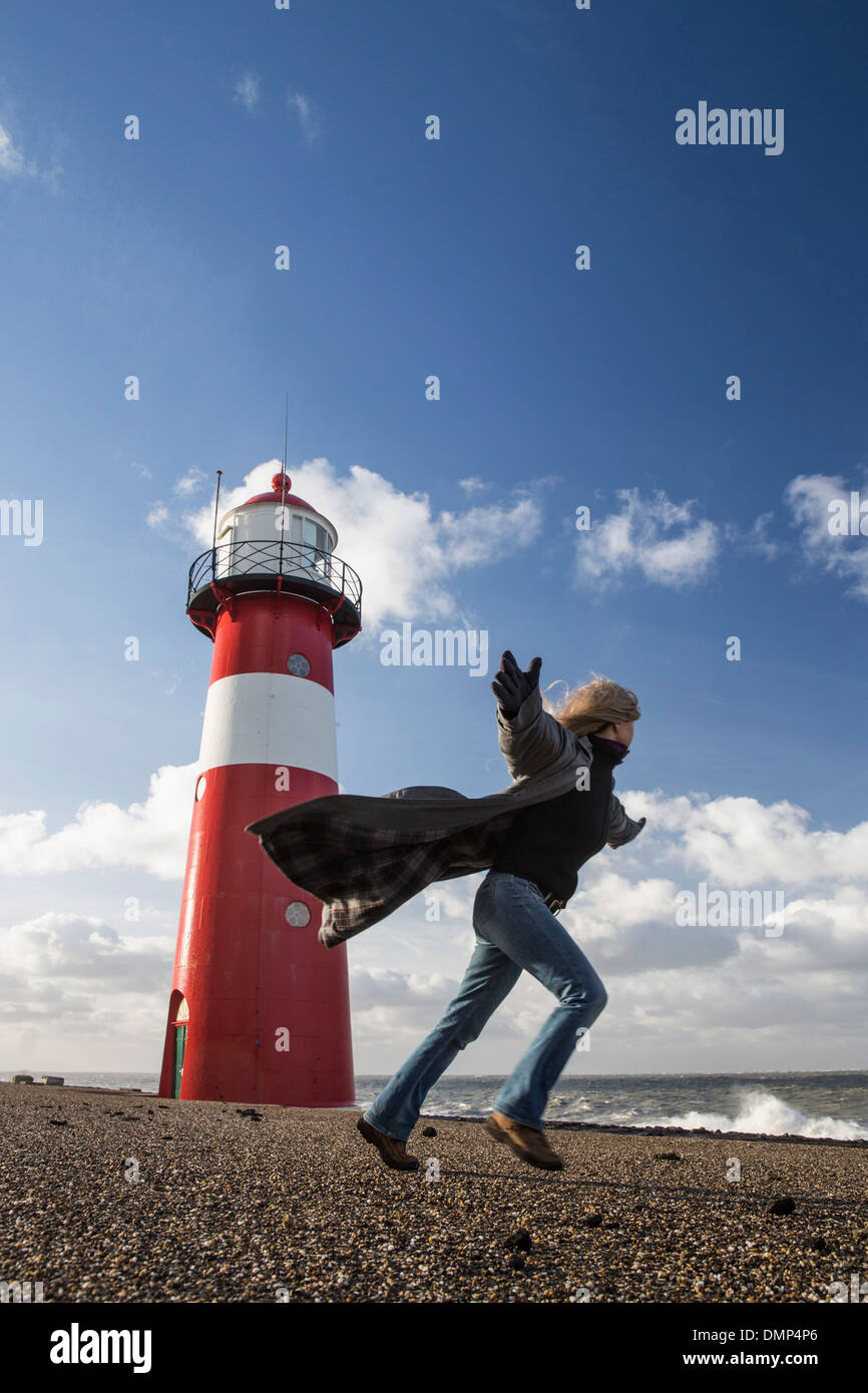 Niederlande, Westkapelle, Leuchtturm am Deich. Frau spielt mit dem Wind bei schweren Sturm Stockfoto