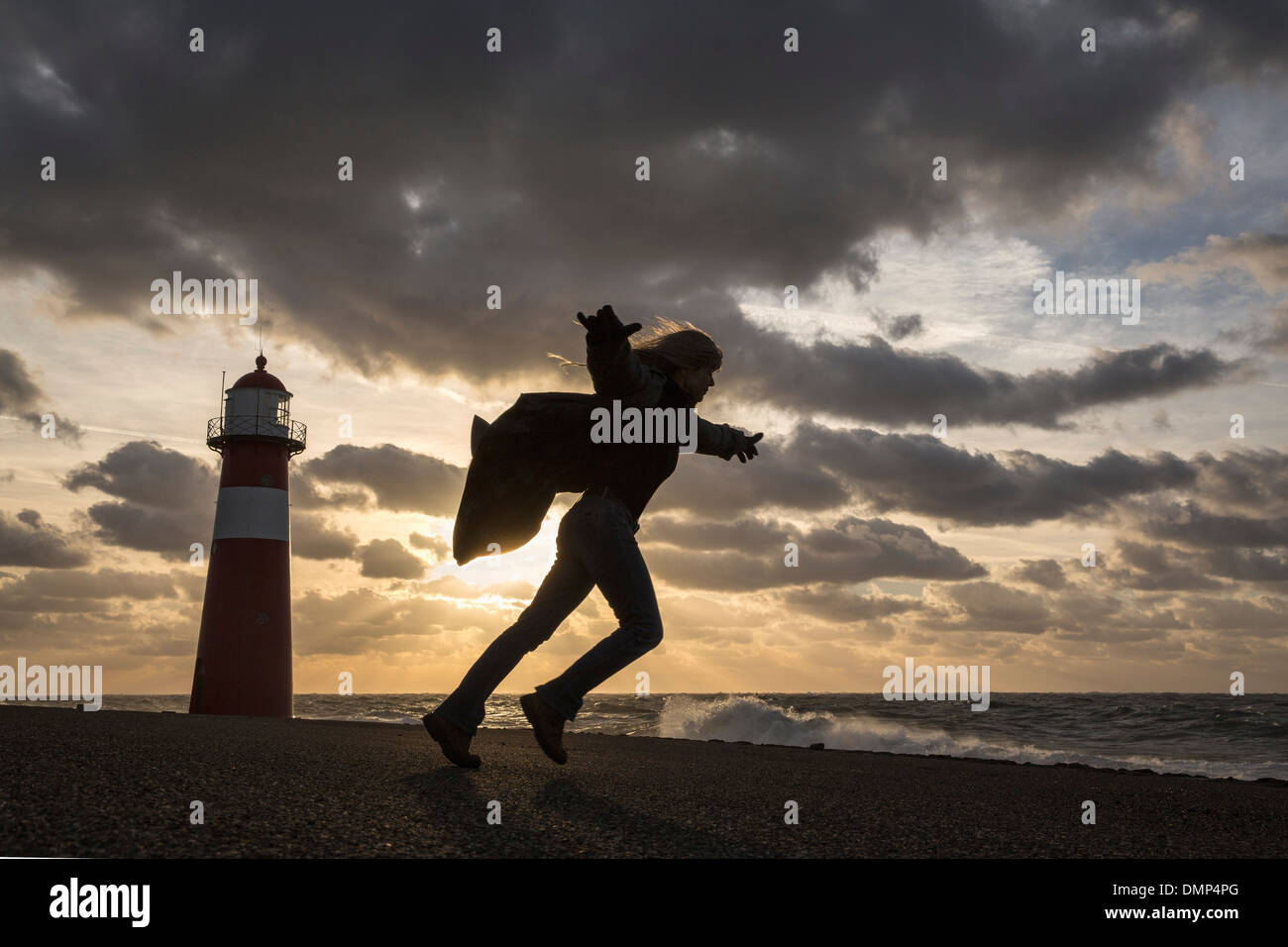 Niederlande, Westkapelle, Leuchtturm am Deich. Frau spielt mit dem Wind bei schweren Sturm Stockfoto