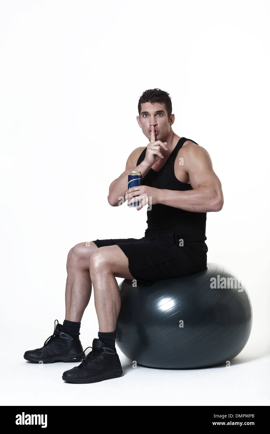 Mann sitzt auf einem Gymnastikball nicht sicher, ob er ein Bier statt Beendigung seines Trainings Stockfoto