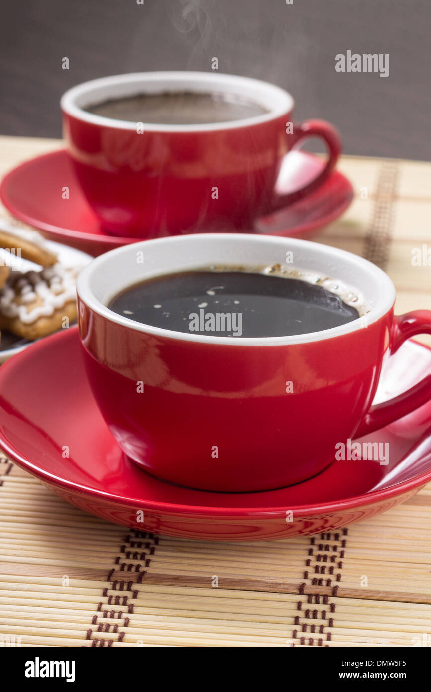 Zwei rote Tassen Kaffee mit Dampf auf Bambus-Hintergrund Stockfoto