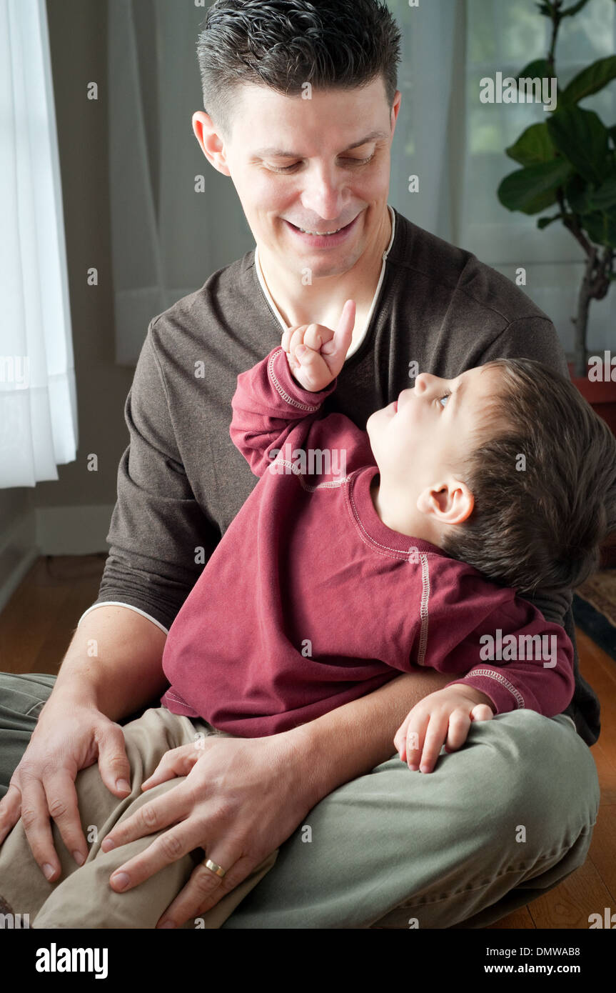 Ein Kind sitzt in des Vaters Schoß, zeigte mit dem Finger auf seinen Vater, die lächelt. Ein Familienporträt. Stockfoto