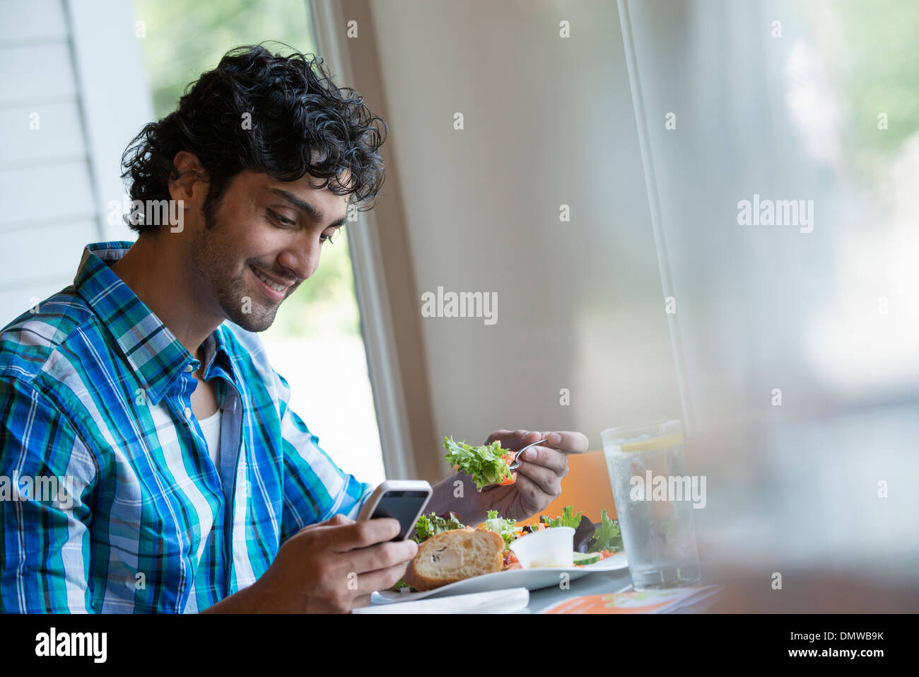 Ein Mann sitzt überprüft seine Telefon und Essen in einem Café. Stockfoto