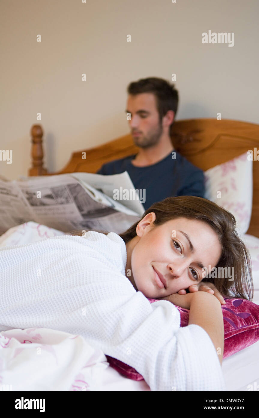 Ein Mann im Bett und eine Frau entspannt lächelnd Zeitung lesen. Stockfoto