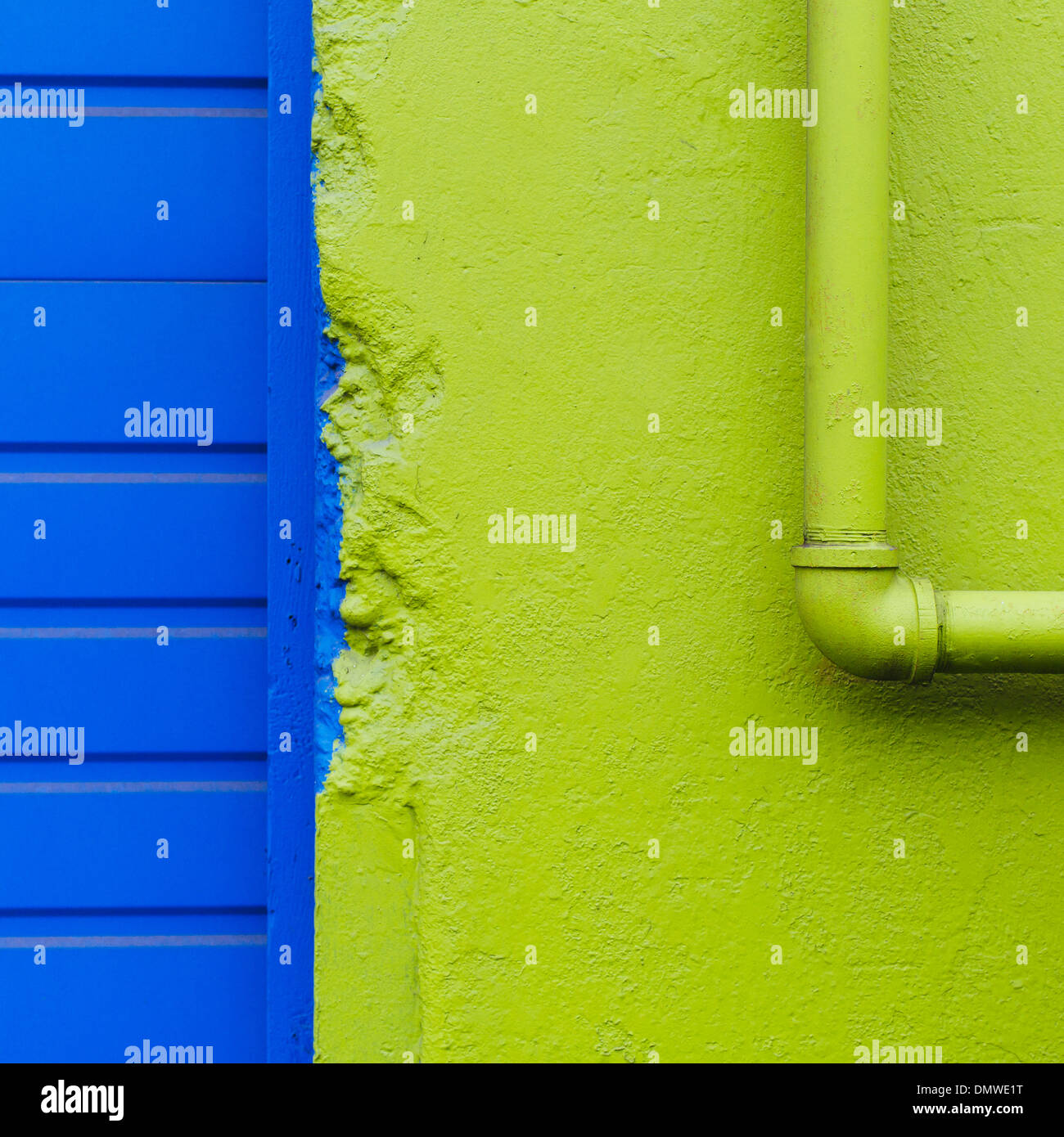Eine grüne Wand und Rohr durch eine blaue Tür. Stockfoto
