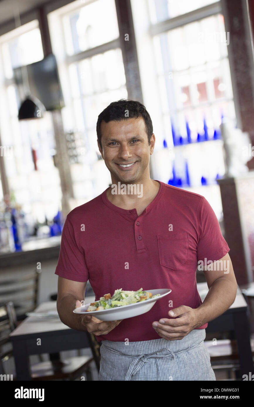 Ein Café-Interieur. Ein Mann in ein Kellner Schürze eine Mahlzeit. Stockfoto
