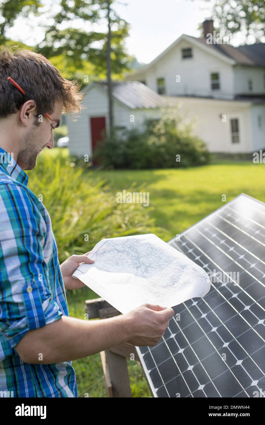 Ein Mann mit einem Plan, um ein Solar-Panel in einem Bauerngarten zu platzieren. Stockfoto