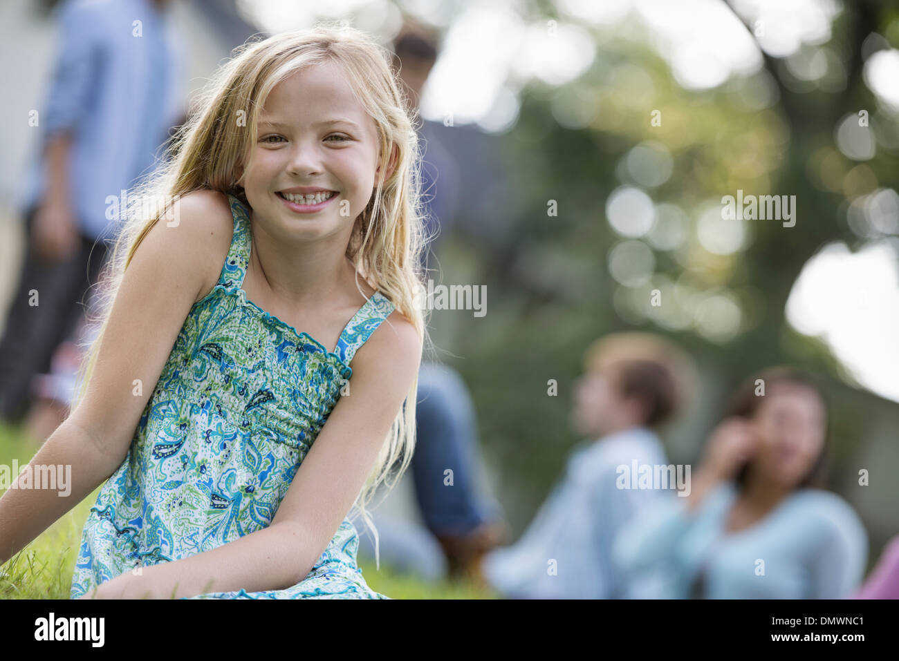 Ein Kind sitzt auf dem Rasen auf einem Sommerfest. Stockfoto