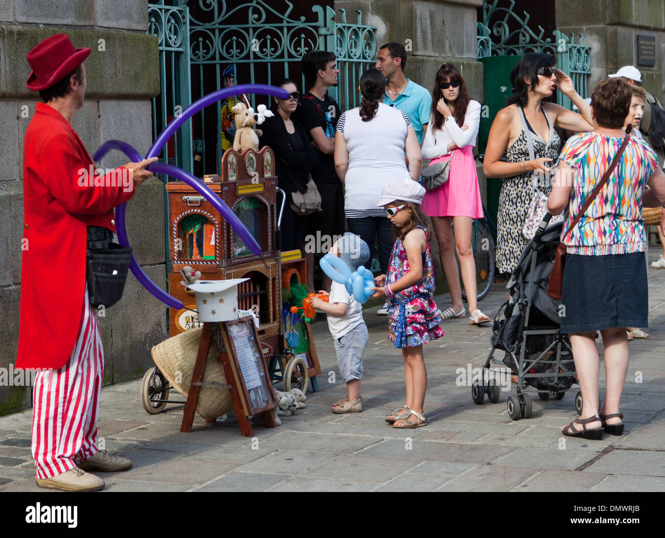 GUERANDE während Markttag mit Straße Entertainer in entkleidet Hosen, roten langen Mantel und Hut Gestaltung lange lila Luftballons Stockfoto