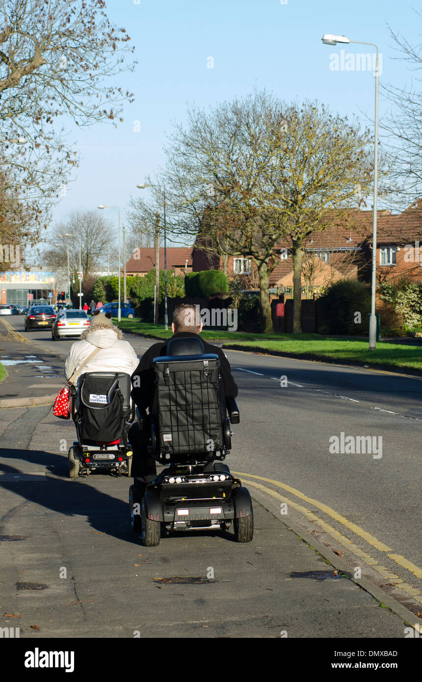 Ältere Menschen mit Scooter fahren entlang einer Fahrbahn in einer Stadt in England. Stockfoto