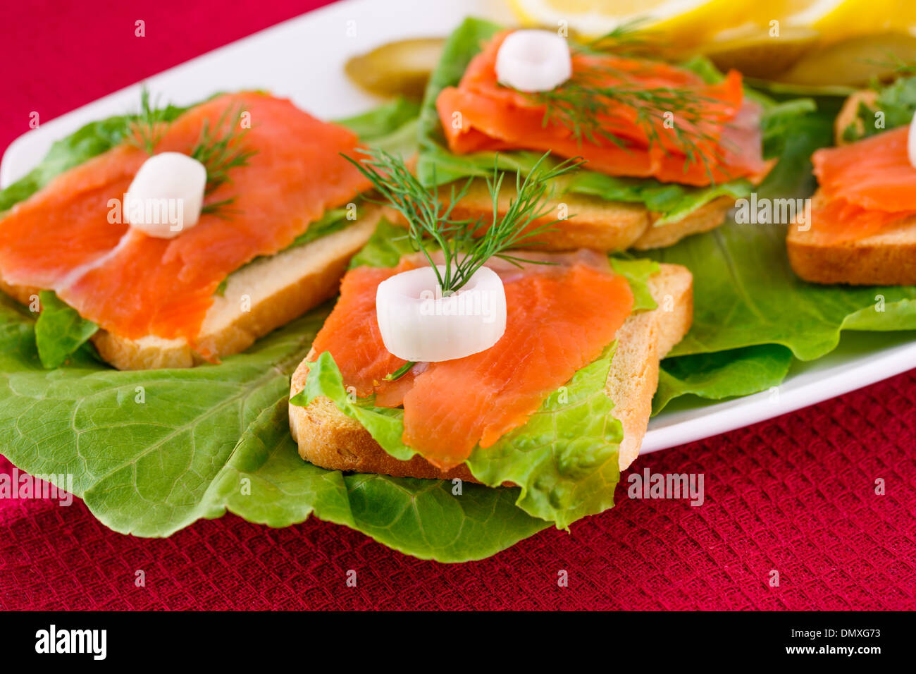 Lachs Sandwiches mit Salat, frische und eingelegte Gurken, Zwiebel, Zitrone auf Platte. Stockfoto