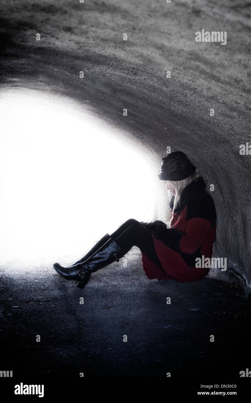 eine Frau in einem roten Mantel sitzt in einem dunklen tunnel Stockfoto