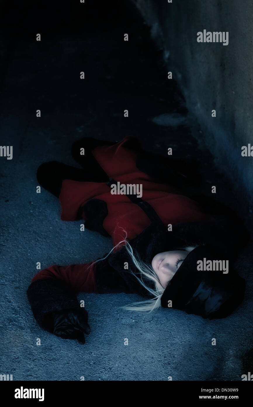 eine Frau in einem roten Mantel ist in einem dunklen Tunnel liegen. Stockfoto
