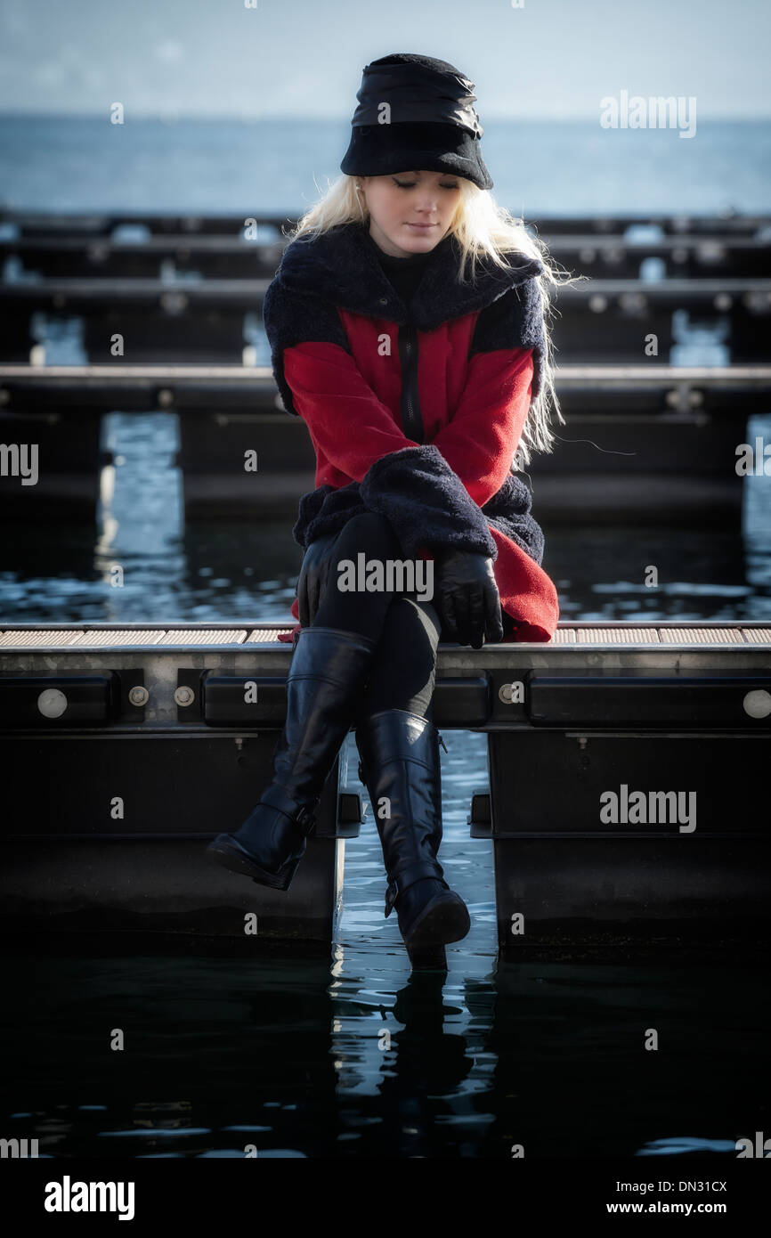 eine Frau in einem roten Mantel sitzt auf einem Steg Stockfoto