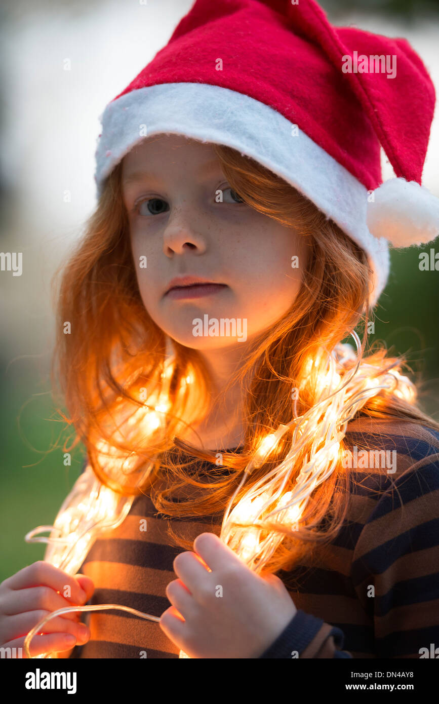 Ein kleines Mädchen gekleidet in einem Santa Hut und Fee Weihnachtsbeleuchtung Stockfoto