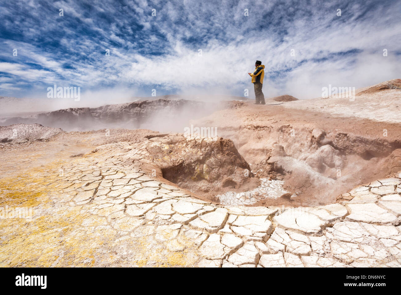 Ein Mann geht in der Nähe einen Krater, umgeben von gerissenen Schlamm und Dampf bei Sol de Manana Geothermie region Stockfoto