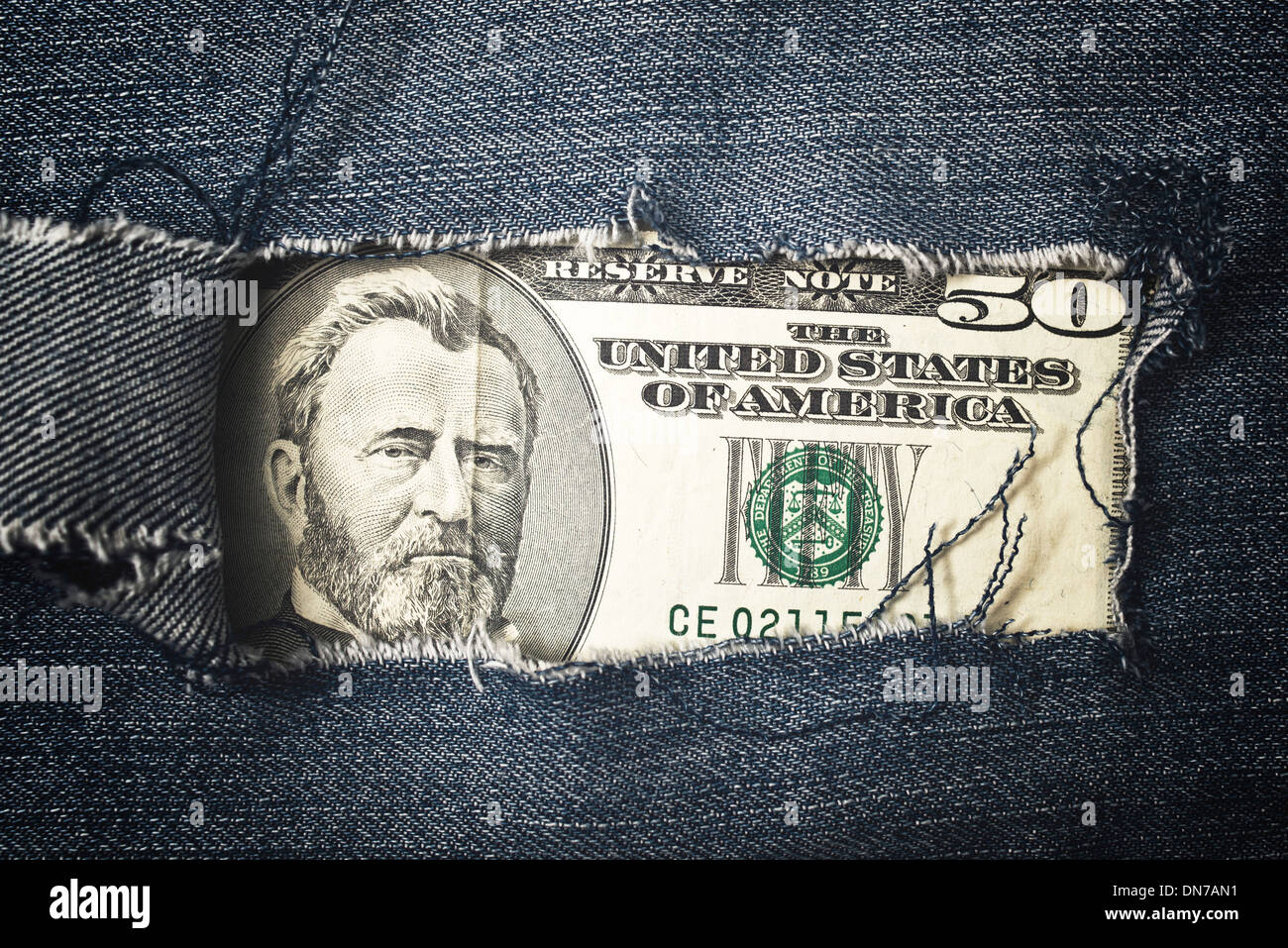 Fünfzig Dollar Bill durch zerrissene Bluejeans Textur. Konzept der amerikanischen Wirtschaft. Stockfoto