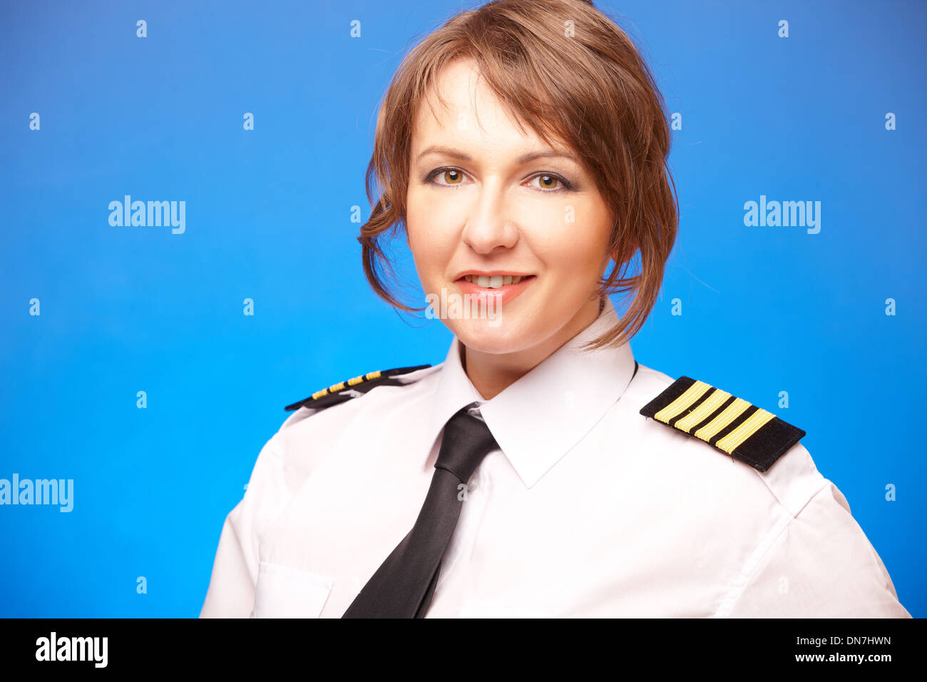 Schöne Frau Pilot in Uniform mit Epauletes, vorausschauend, stehend auf blauem Hintergrund. Stockfoto