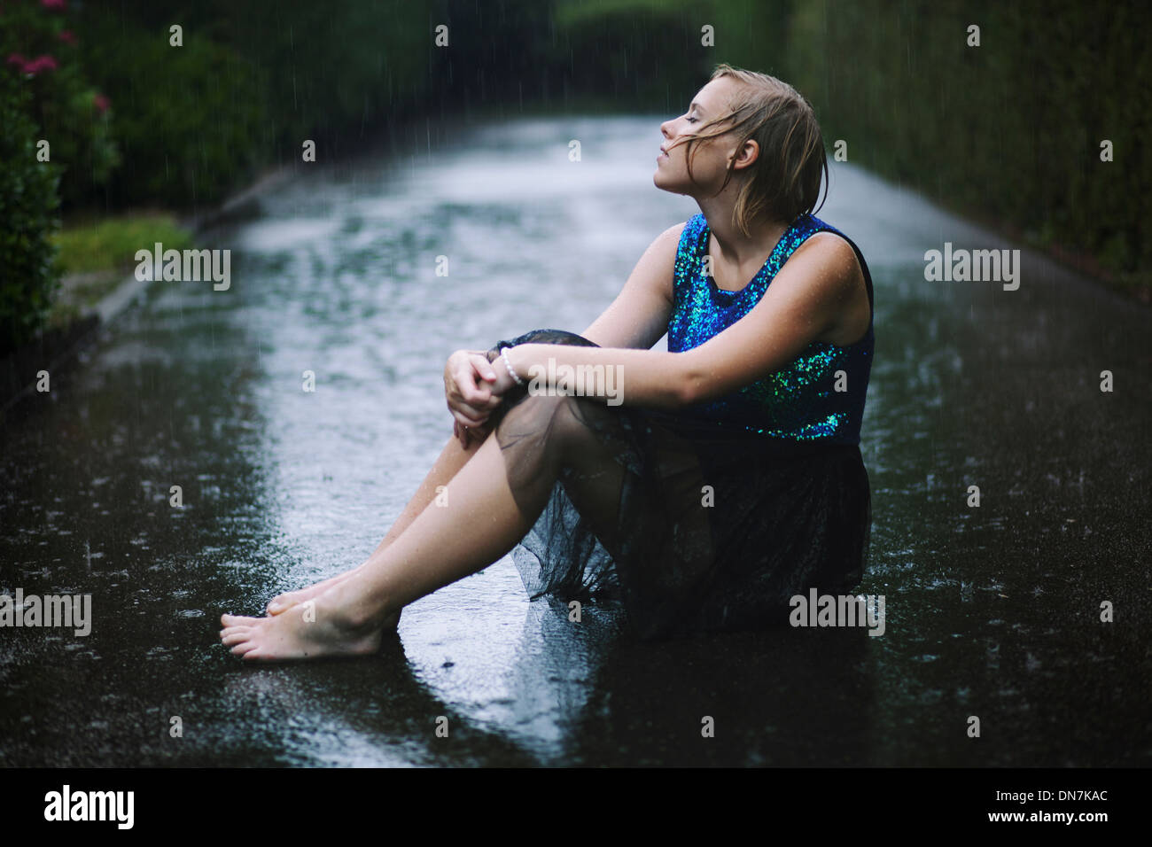Junge Frau sitzt im Regen auf der Straße Stockfoto