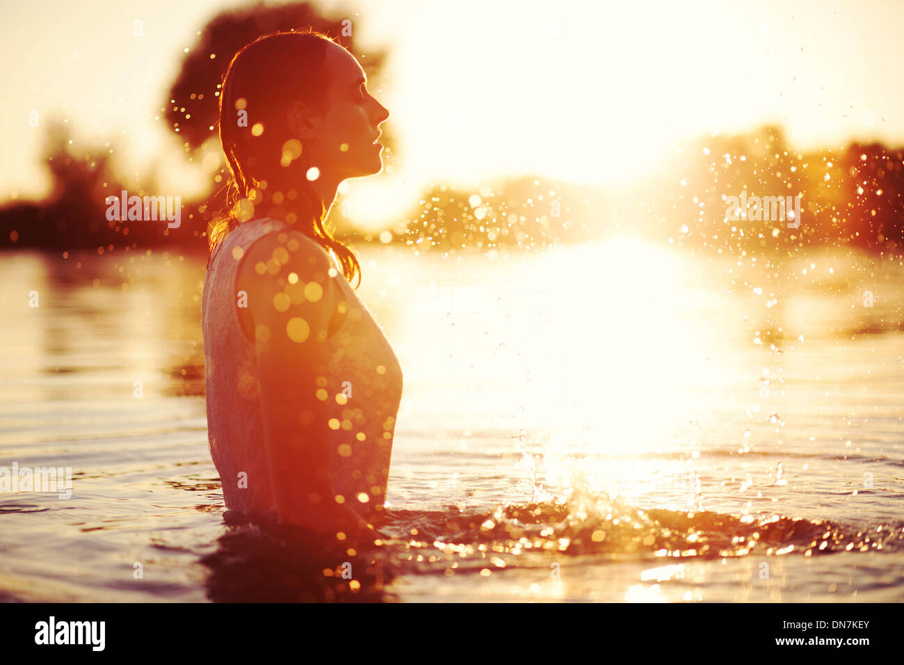 Junge Frau bei Sonnenuntergang im See plantschen mit Wasser Stockfoto