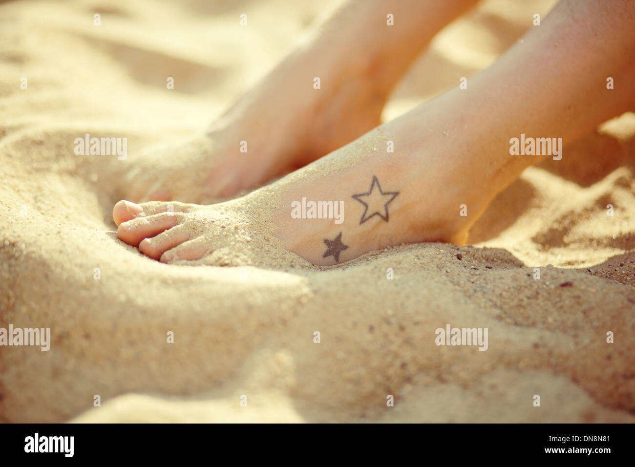 Füße mit Tatoo am Sandstrand Stockfoto