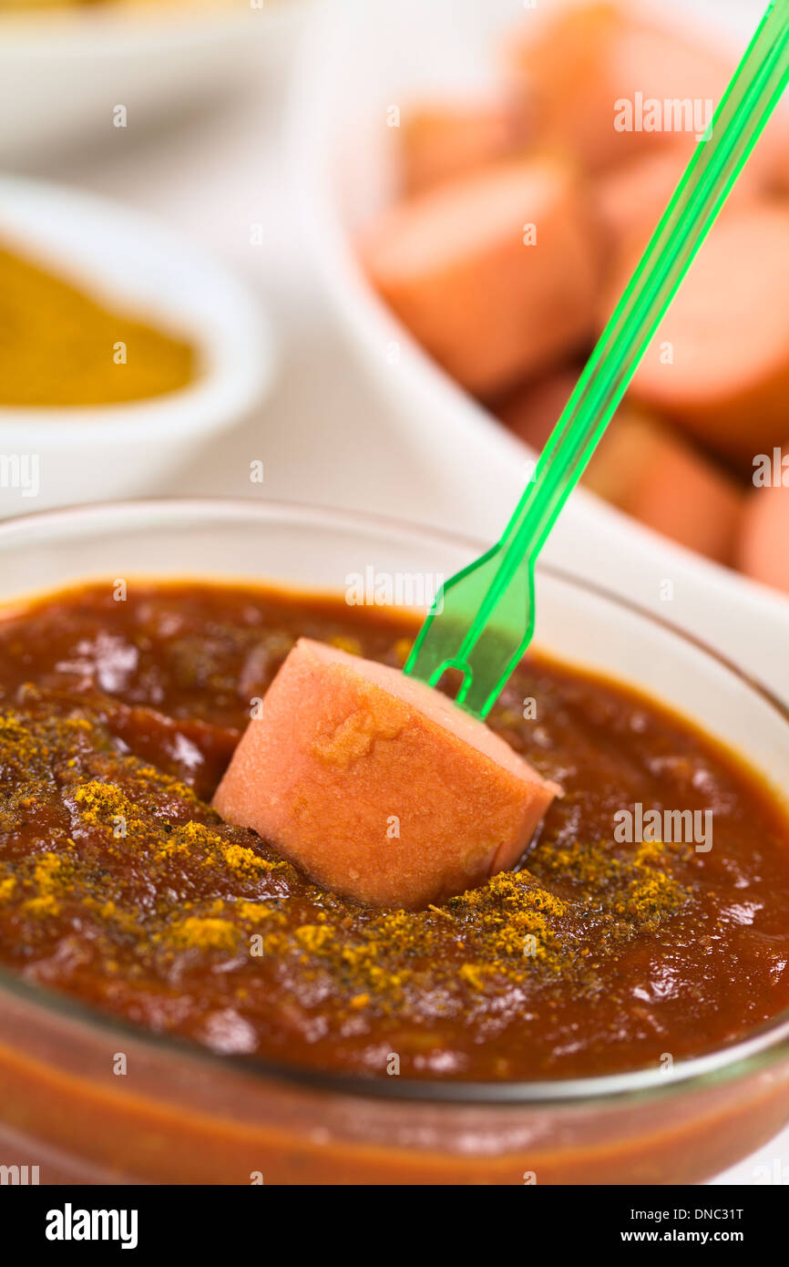 Gebratene Wurst auf Kunststoff Partei Gabel tauchte in Curry-Ketchup-Sauce, gebratene Wurst Stücke und Currypulver in den Rücken Stockfoto