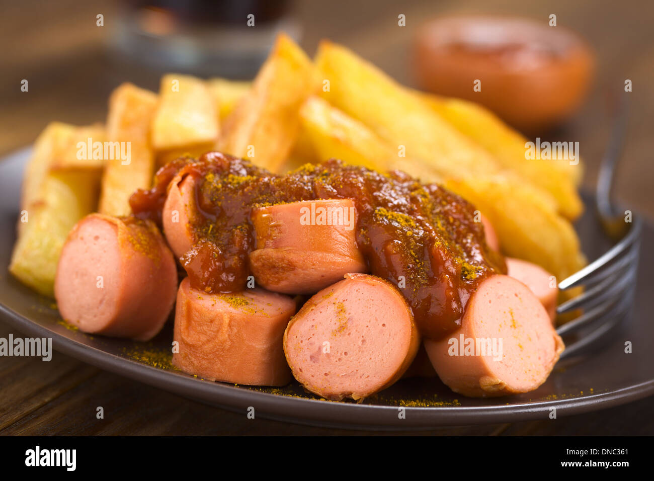 Deutsche Fast-Food genannt Currywurst serviert mit Pommes Frites auf einem Teller mit Gabel Stockfoto