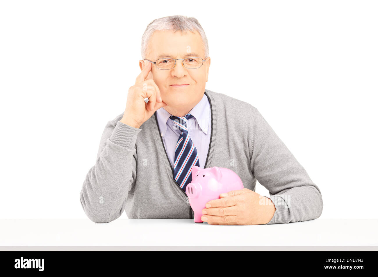 Mann mittleren Alters posiert auf einem Tisch mit Sparschwein Stockfoto