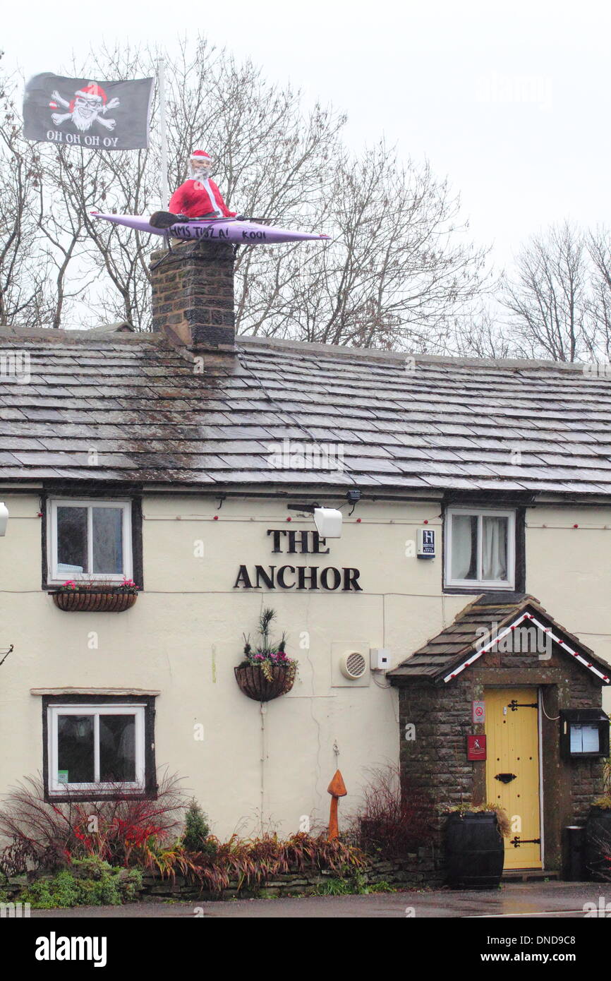 Tideswell, Derbyshire, UK.  23. Dezember 2013.  Santa sitzt in einem Kanu, genannt "HMS Tidza" auf dem Dach des The Anchor Inn, einer Gastwirtschaft 15. Jahrhundert als strömendem Regen und starkem Wind fegen über den Peak District.  Tideswell ist von den lokalen Bewohnern liebevoll als Tidza bezeichnet. Bildnachweis: Deborah Vernon/Alamy Live-Nachrichten Stockfoto