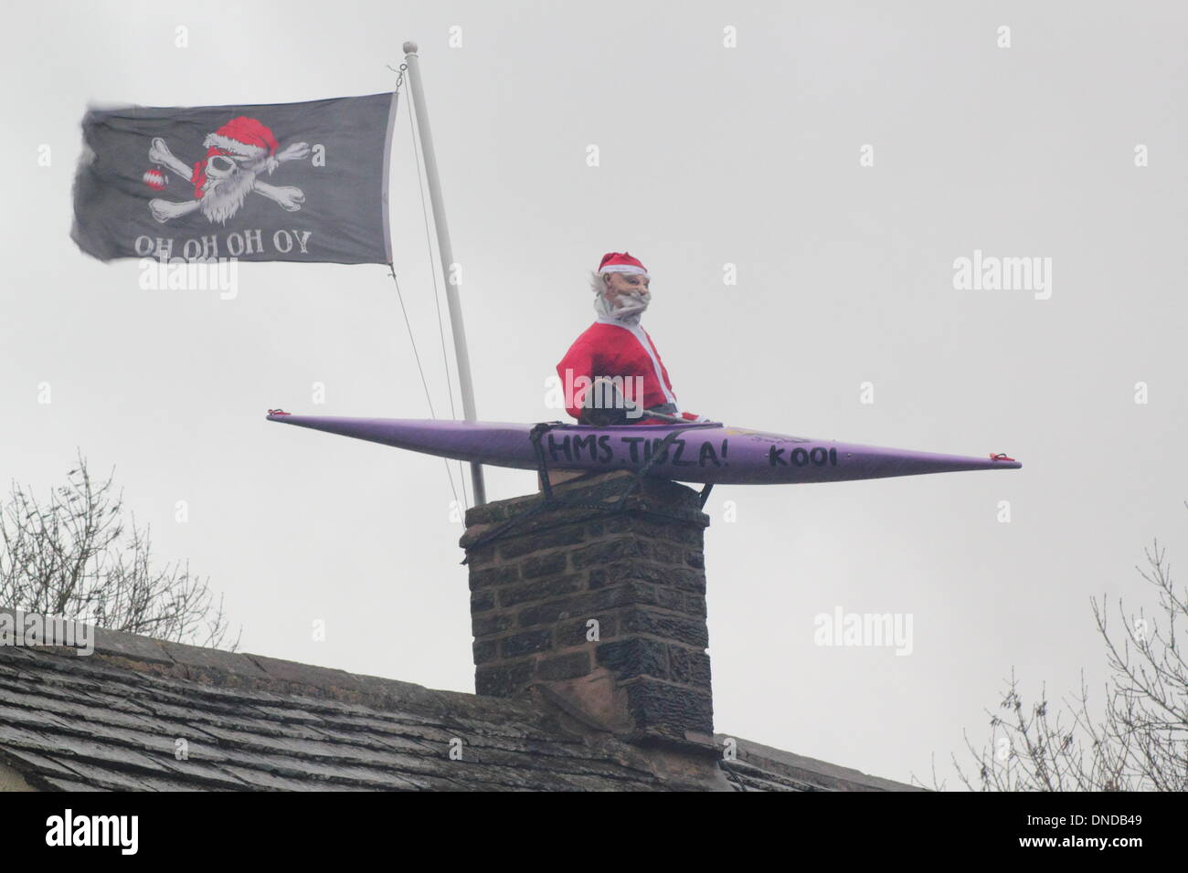 Tideswell, Derbyshire, UK.  23. Dezember 2013.  Santa sitzt in einem Kanu, genannt "HMS Tidza" auf dem Dach des The Anchor Inn, einer Gastwirtschaft 15. Jahrhundert als strömendem Regen und starkem Wind fegen über den Peak District.  Tideswell ist von den lokalen Bewohnern liebevoll als Tidza bezeichnet. Stockfoto