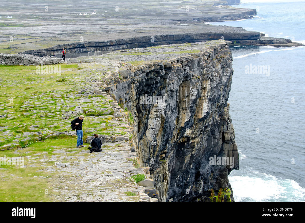 Touristen am steilen Felsen neben prähistorischen Steinkastell Dun Aengus, Inishmore (Inis Mor), Aran Islands, Irland Stockfoto