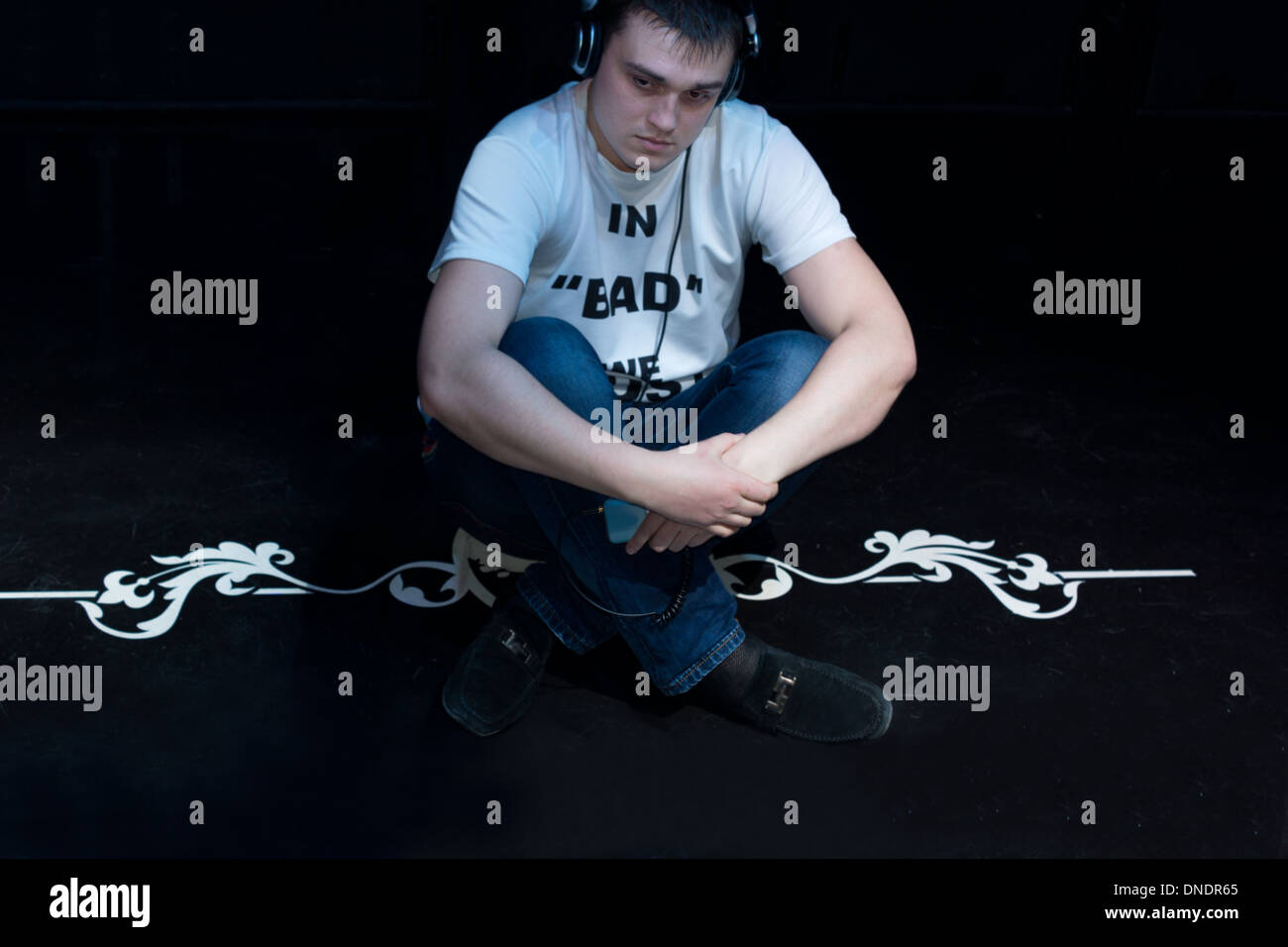 Zufriedener junge Mann sitzt Kreuz Beinen Musikhören auf seine Kopfhörer als er lockert und in der Dunkelheit entspannt Stockfoto