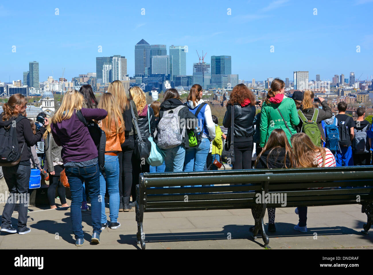 Eine Gruppe von Mädchen und Jungen sieht die Studenten einen Bildungsbesuch im Greenwich Park & Observatory mit Blick auf Canary Wharf am sonnigen Frühlingstag London UK Stockfoto