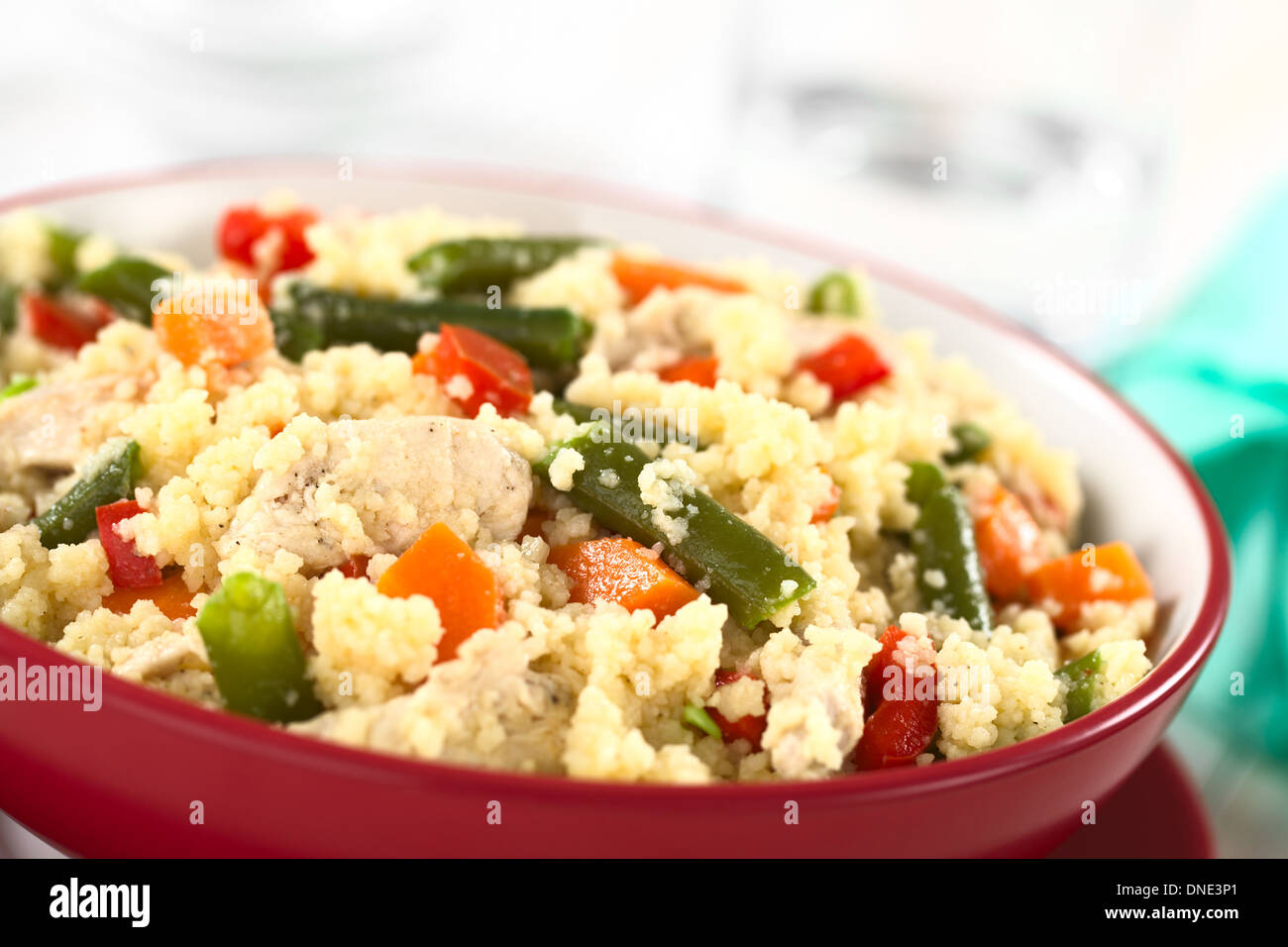 Couscous mit Huhn, grüne Bohnen, Karotten und Paprika serviert in einer roten Schale Stockfoto