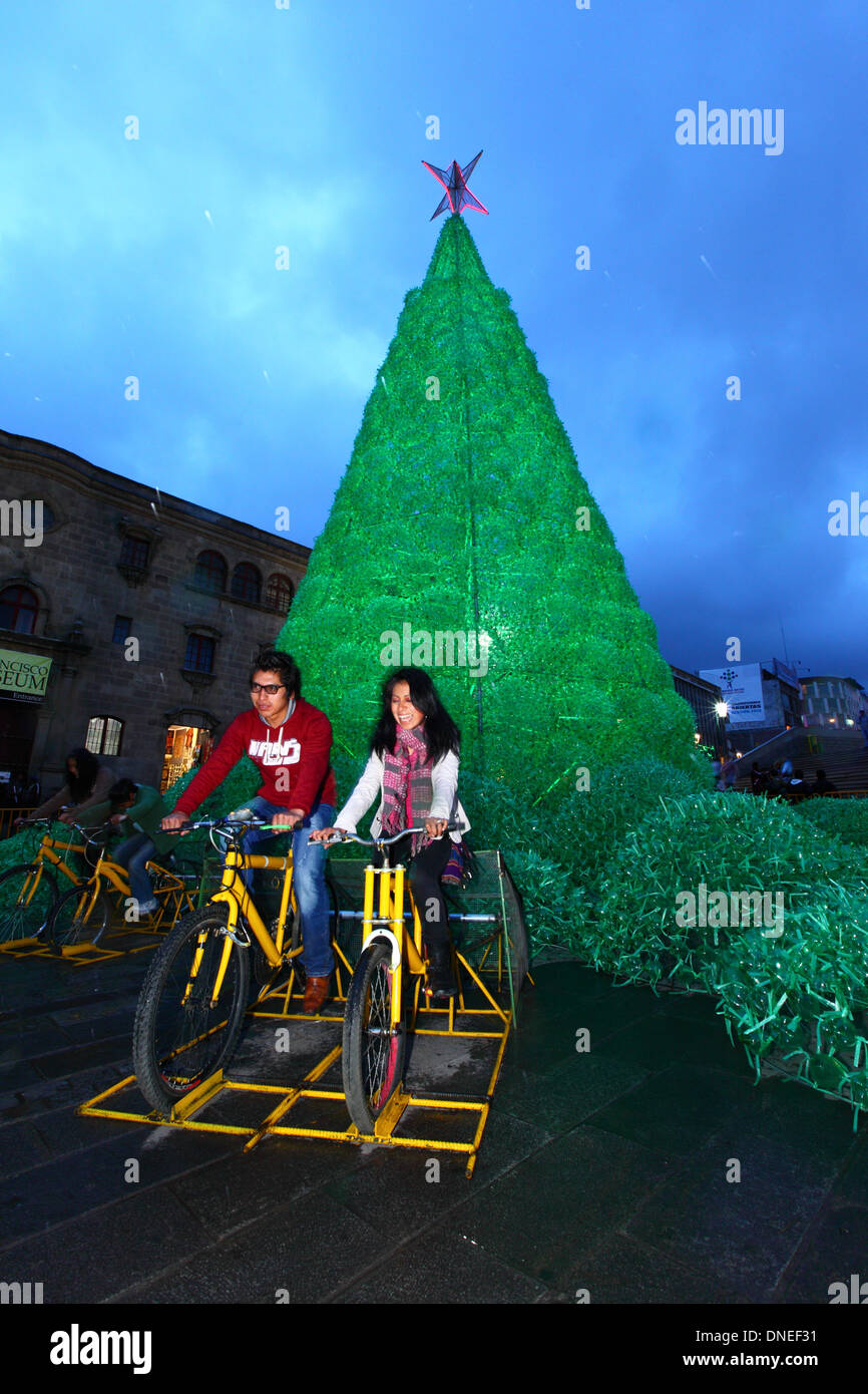 La Paz, Bolivien. 24. Dezember 2013. Einheimischen Pedal auf Fahrrädern verbunden, Batterien, elektrischen Energie für die Beleuchtung auf eine ökologische Weihnachtsbaum im Plaza San Francisco bieten. Der Baum ist mehr als 15m hoch, enthält ca. 50.000 recycelten Kunststoff-Getränkeflaschen und war ein Projekt konzipiert und geplant von der Stadtverwaltung von La Paz. Bildnachweis: James Brunker / Alamy Live News Stockfoto