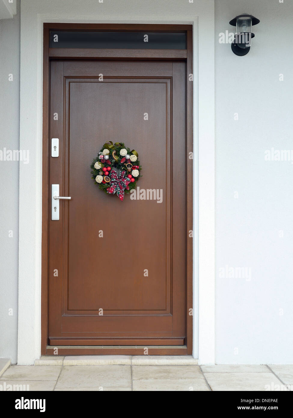 Adventskranz mit Dekorationen und Schleife an der Holztür angebracht Stockfoto