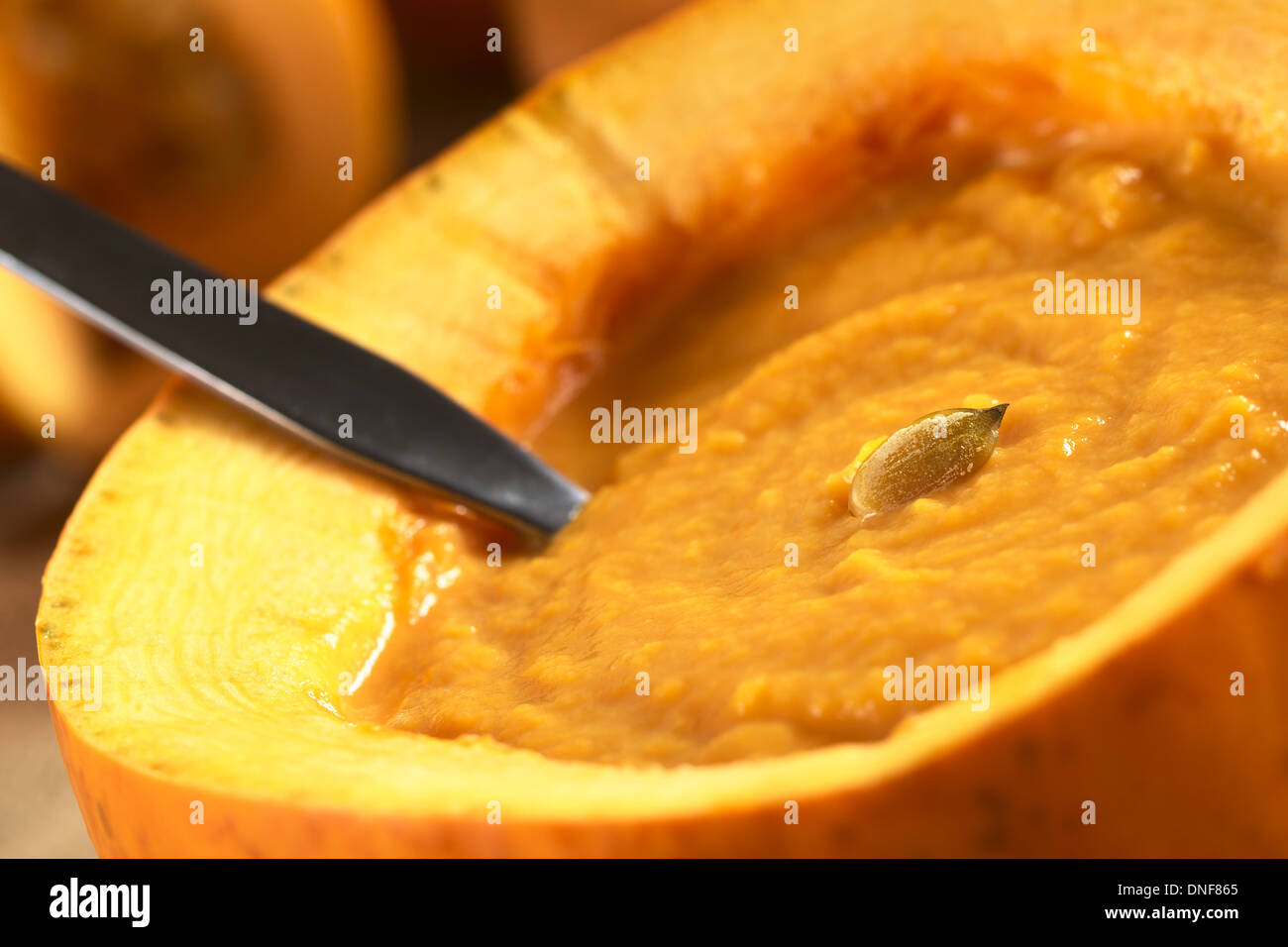 Frische, cremige Kürbissuppe in einen Kürbis mit einem Löffel serviert und garniert mit einem Kürbis Samen Stockfoto