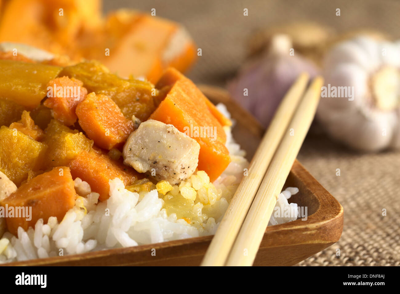 Huhn, Kürbis und Süßkartoffeln Curry serviert auf Reis in Holzplatte mit Stäbchen Stockfoto