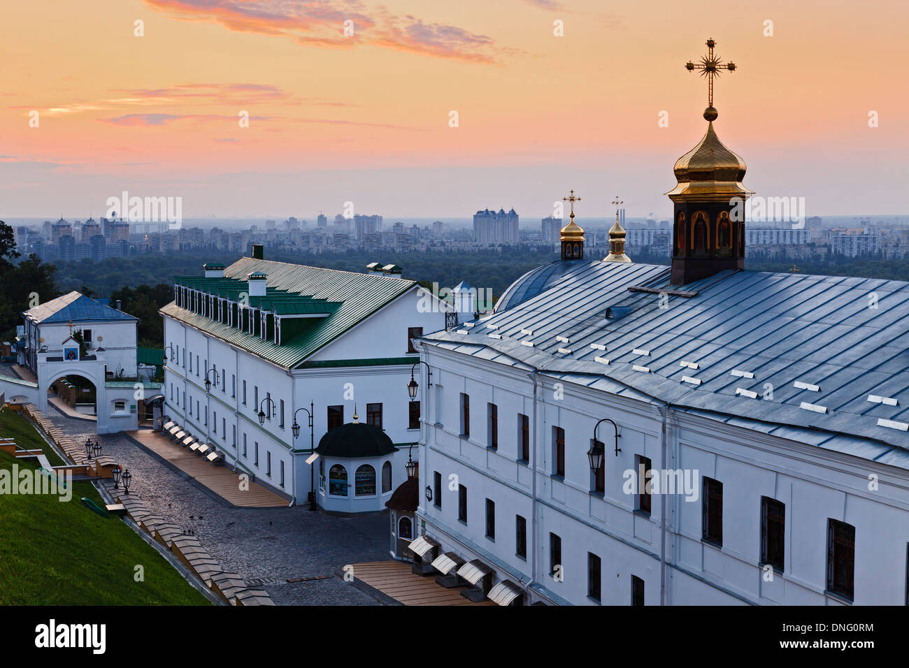 Ukraine Kiew Pechers Lavra internen Gebäude mit Kuppeln und Kreuz bei Sonnenaufgang gegen entfernte moderne Stadtgebäude Stockfoto