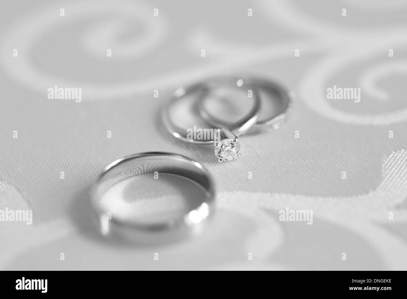 Drei Ringe: Engagement mit Diamanten und zwei Trauringe auf eine Tischplatte. Schwarz / weiß Fotografie. Stockfoto