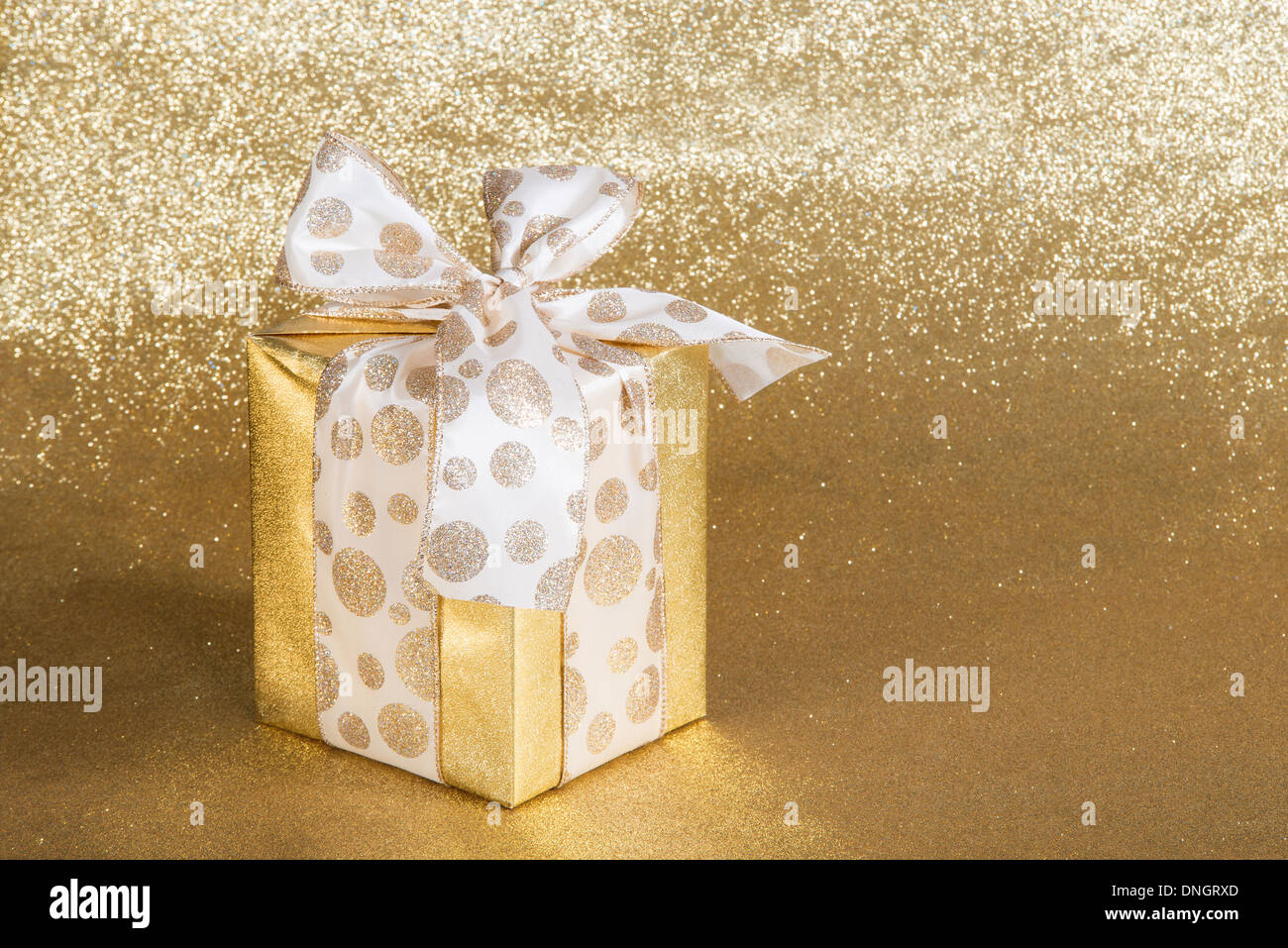 Goldenen Geschenk verpackt mit gepunkteten Schleife über glitzernden goldenen Hintergrund Stockfoto