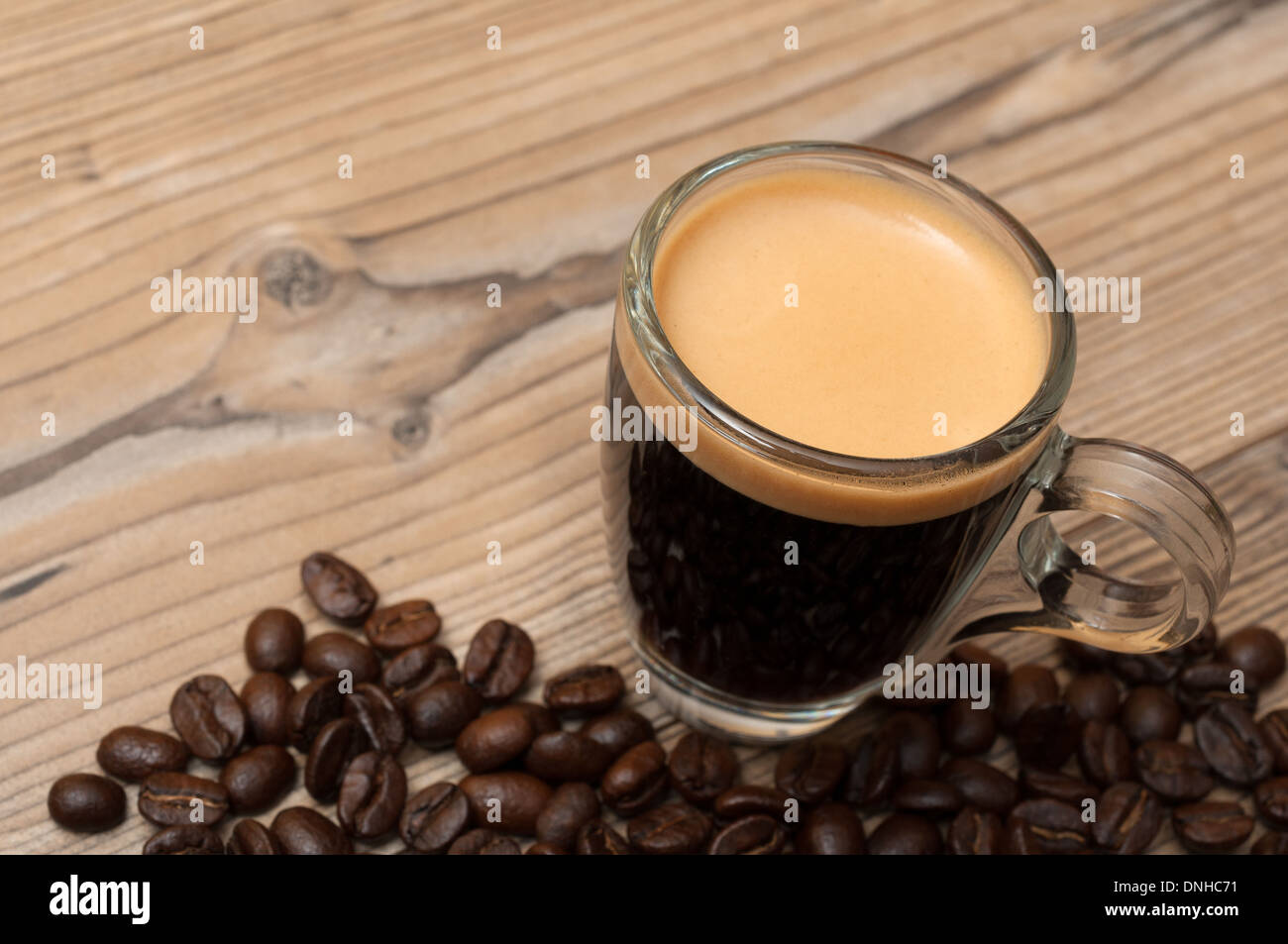 Glastasse Espresso auf Holztisch mit Kaffeebohnen - geringe Schärfentiefe Stockfoto