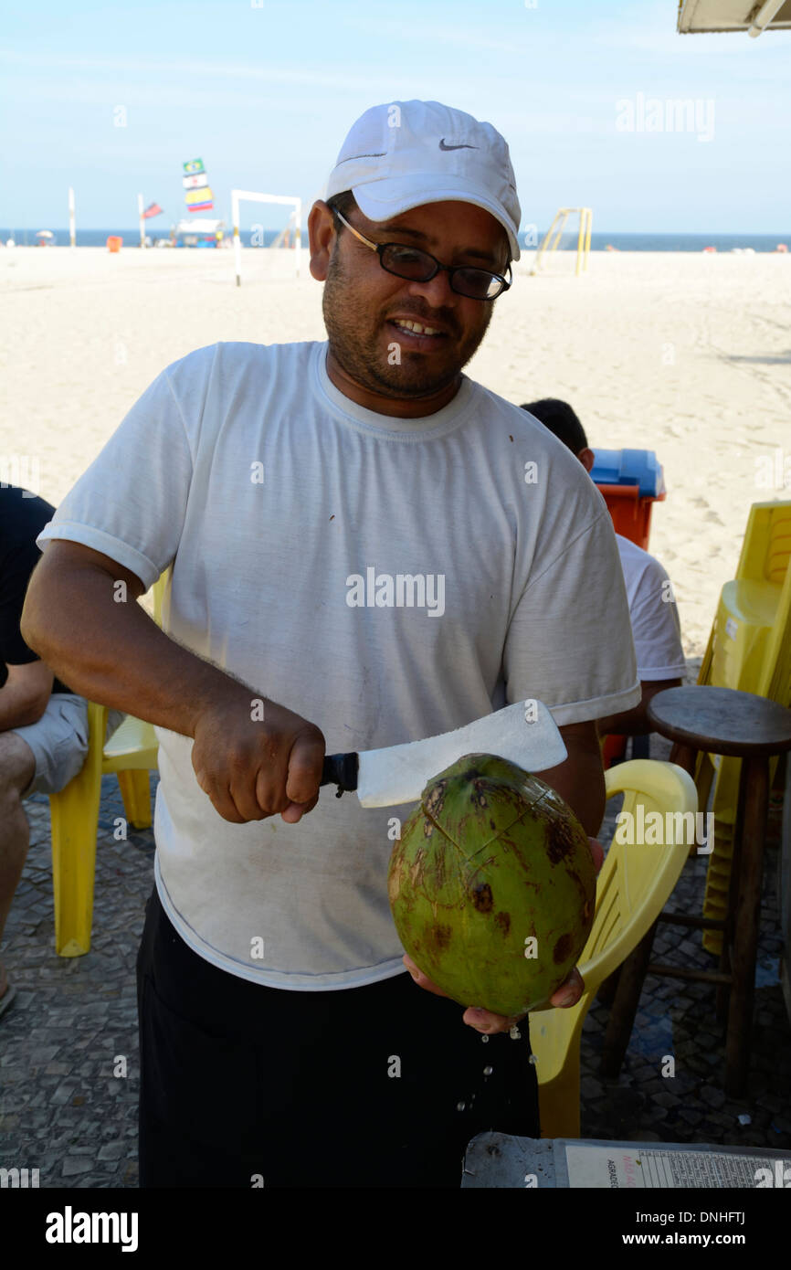 Eine Kokosnuss-Verkäufer hacken eine Kokosnuss für einen Kunden, die Milch zu trinken, am Strand der Copacabana in Rio De Janeiro, Brasilien Stockfoto