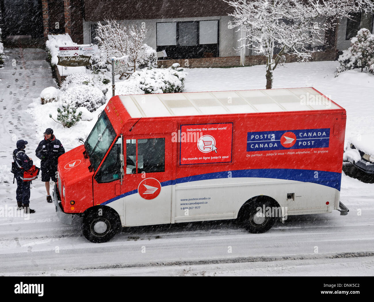 E-Mail-Übermittlung an einem verschneiten Tag in Vancouver. Briefträger spricht kurz mit einem anderen Canada Post-Arbeiter in einem Lieferwagen. Stockfoto