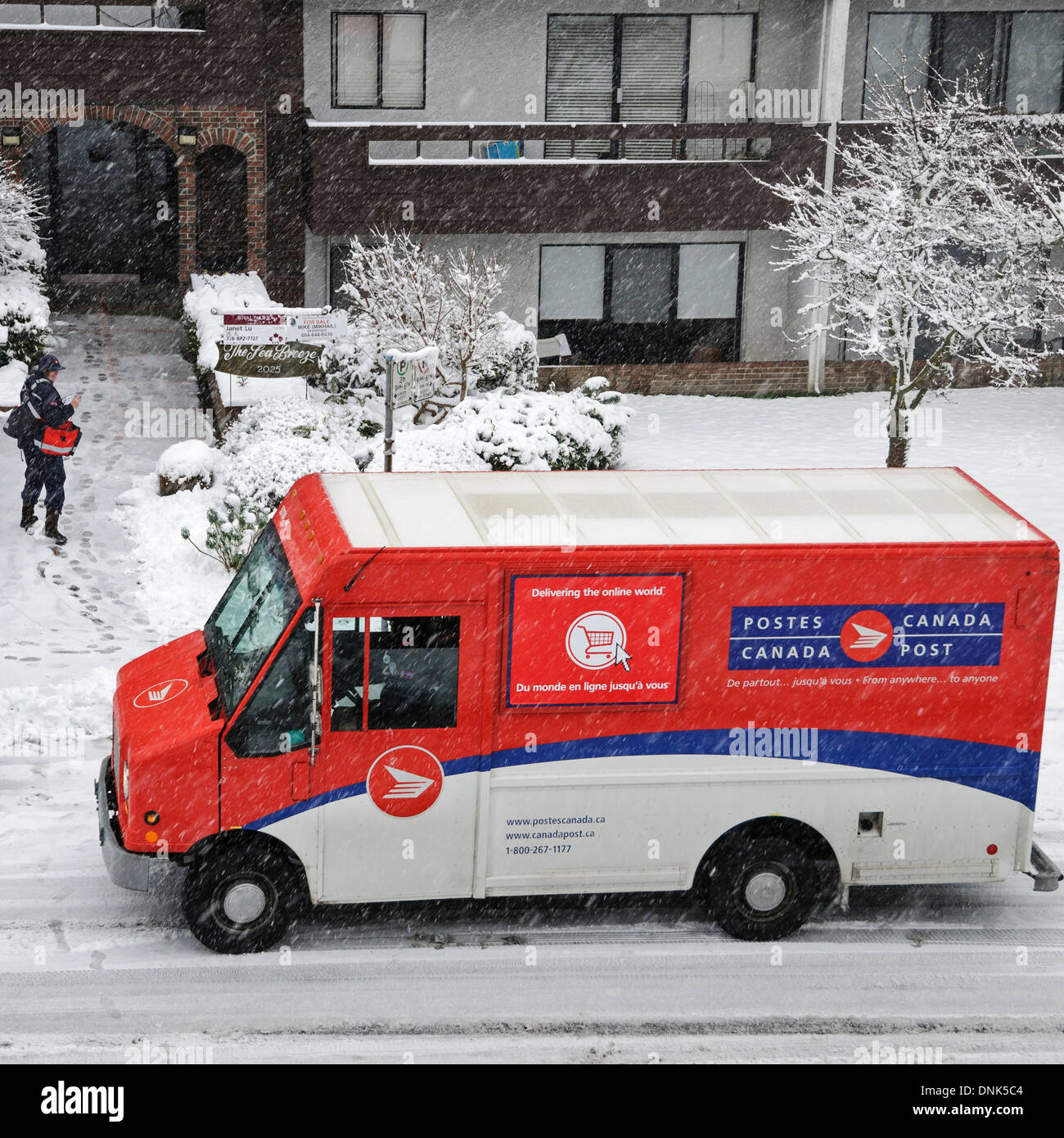 E-Mail-Übermittlung an einem verschneiten Tag in Vancouver. Briefträger spricht kurz mit einem anderen Canada Post-Arbeiter in einem Lieferwagen. Stockfoto